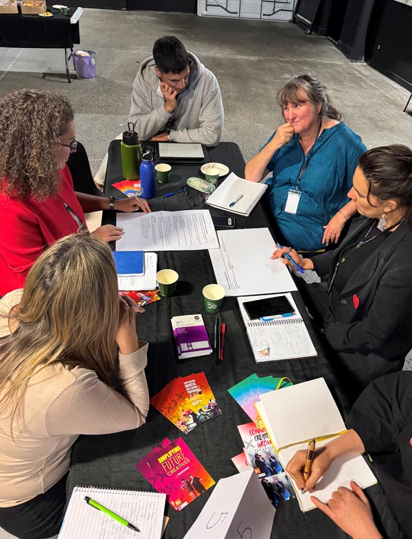 A group of funders and creative space leaders sit around a table discussing funding challenges and solutions